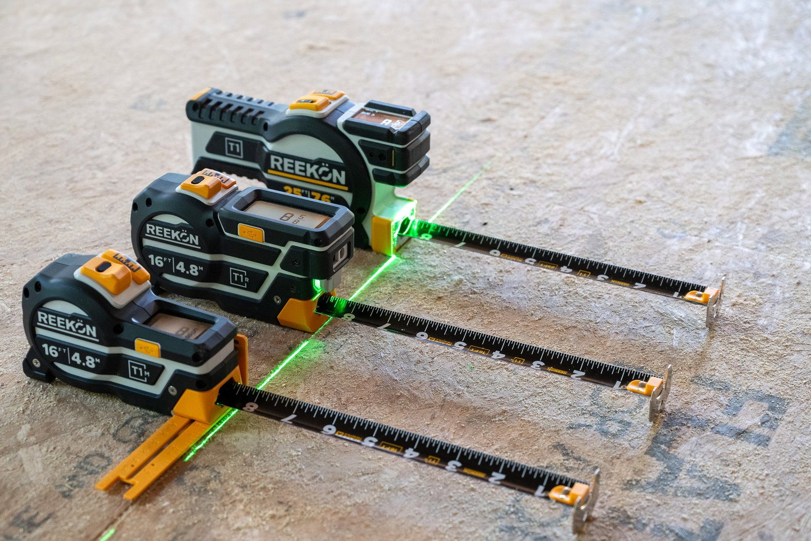 REEKON T1M, T1R, and T1 digital tape measures on OSB with a green laser across the blades